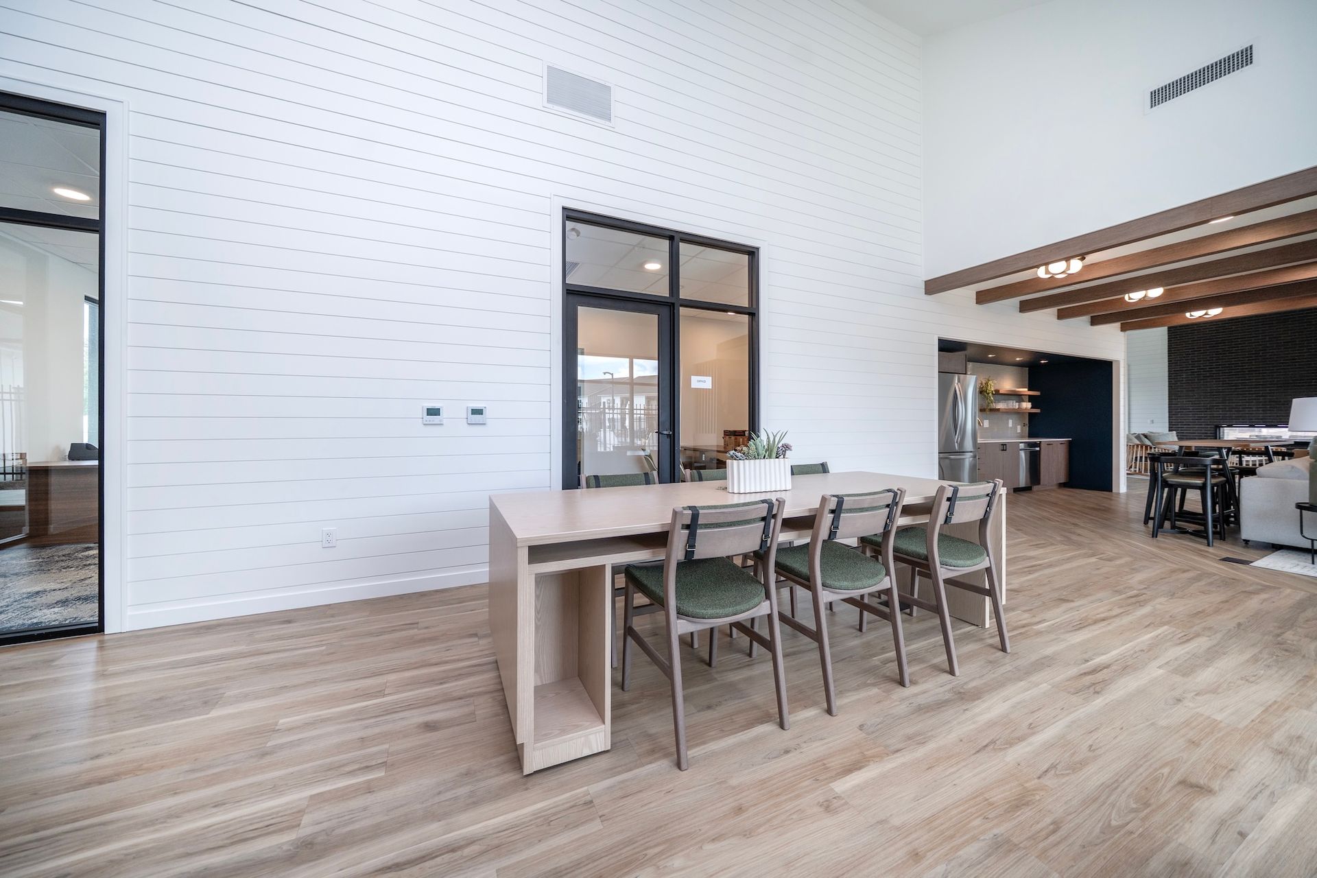 Modern office space with a large table, chairs, wood floor, white brick wall, and a glass door.