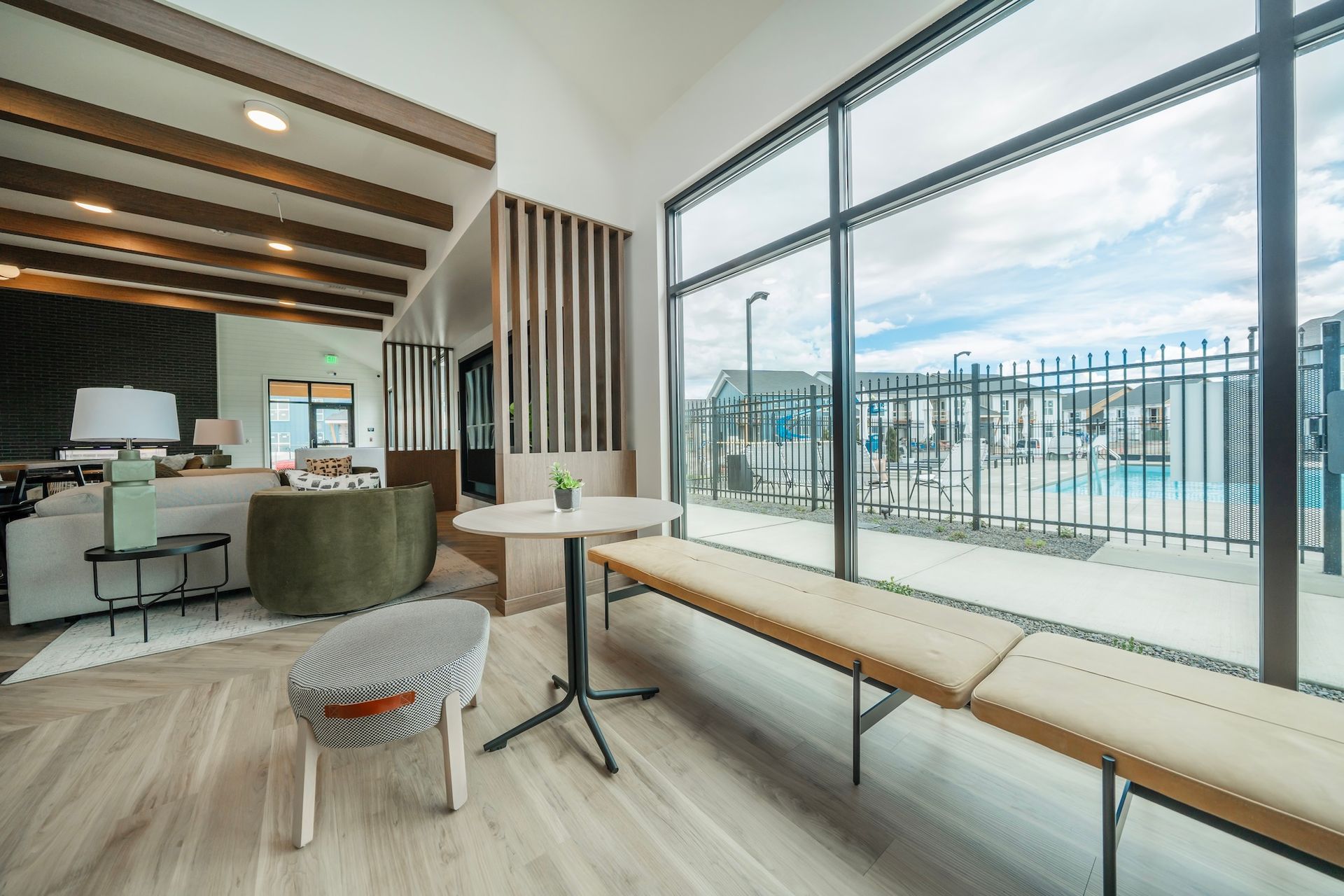 Modern interior with a view of a pool. Features include wooden beams, large windows, and seating areas.