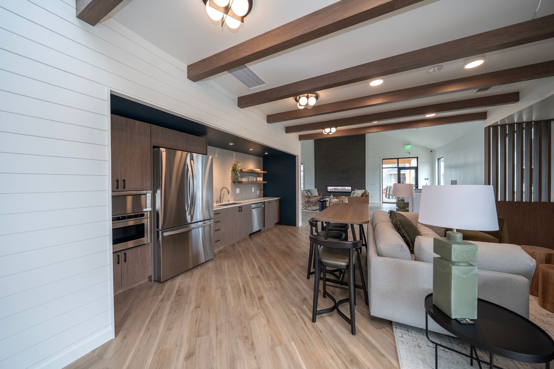 Modern lounge with kitchen, fridge, seating, and wooden beams.