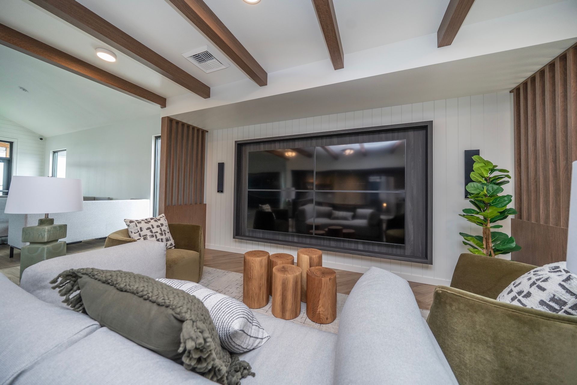 Living room with a large mounted TV, white couch, wooden beams, and green accents.