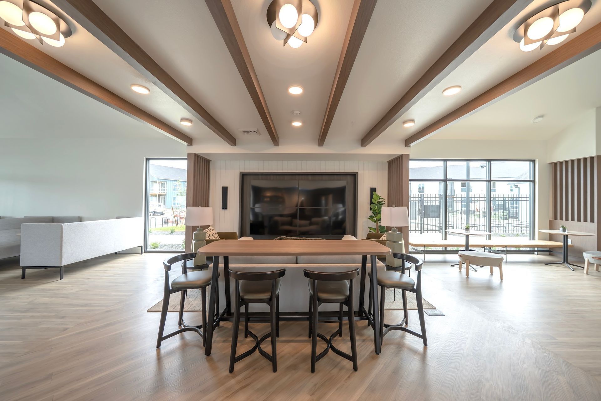 A modern lounge with a central table and chairs, a fireplace, and large windows.