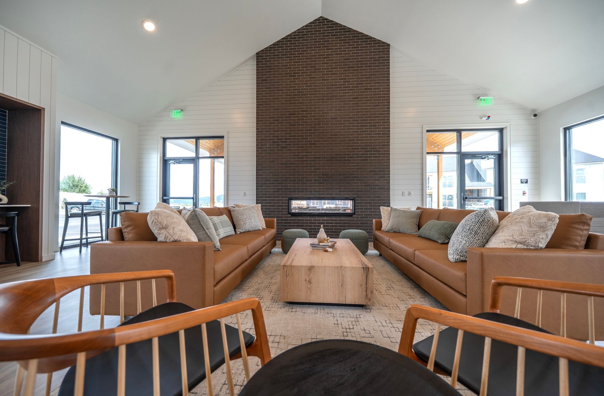 Lounge with brown leather sofas, wood chairs, fireplace, windows, and a light-colored rug.