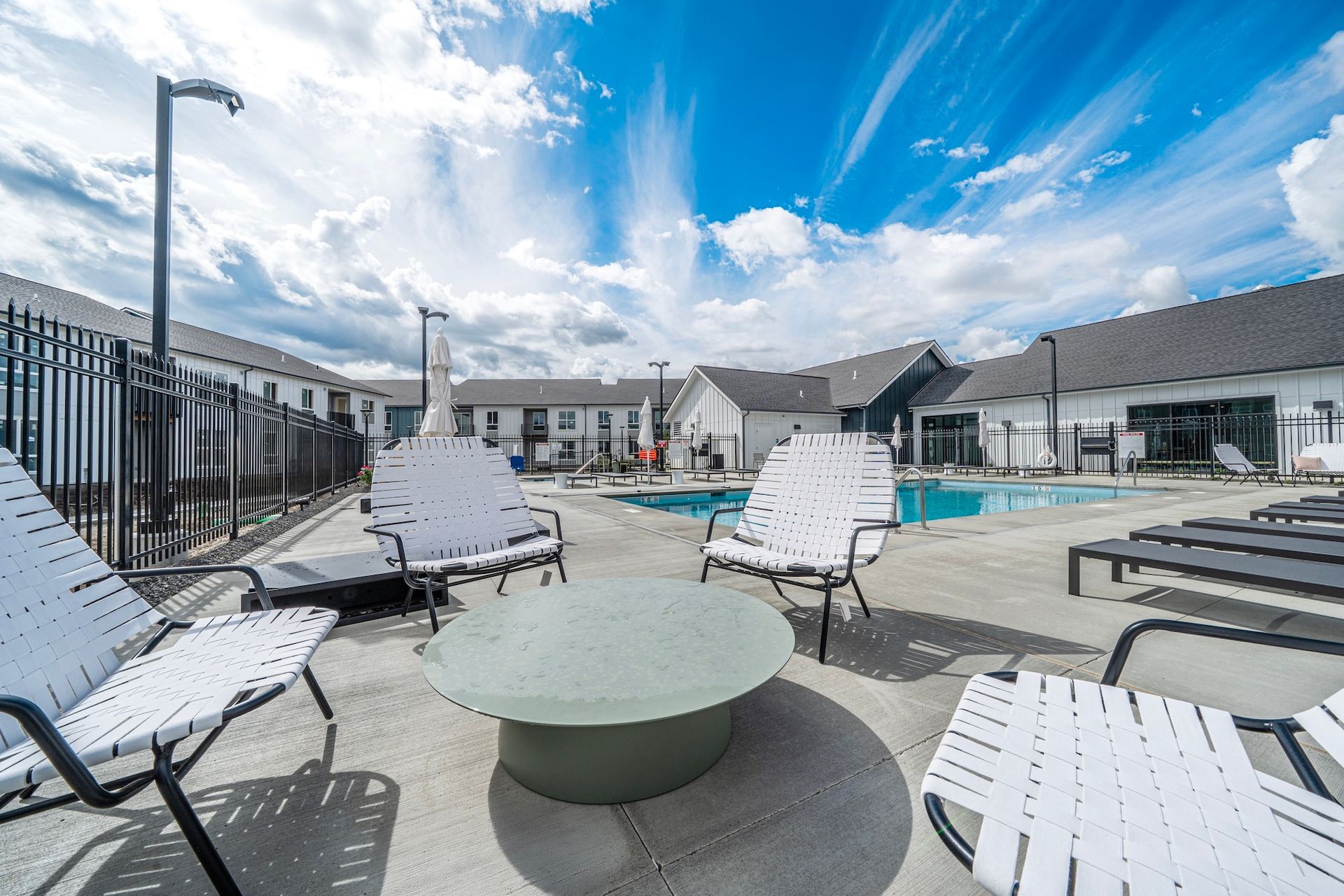 Poolside seating area with white chairs, fire pit, pool, and blue sky.