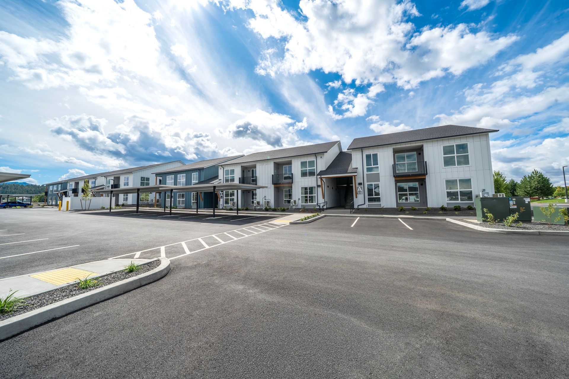 Apartment complex with parking, blue sky with clouds.