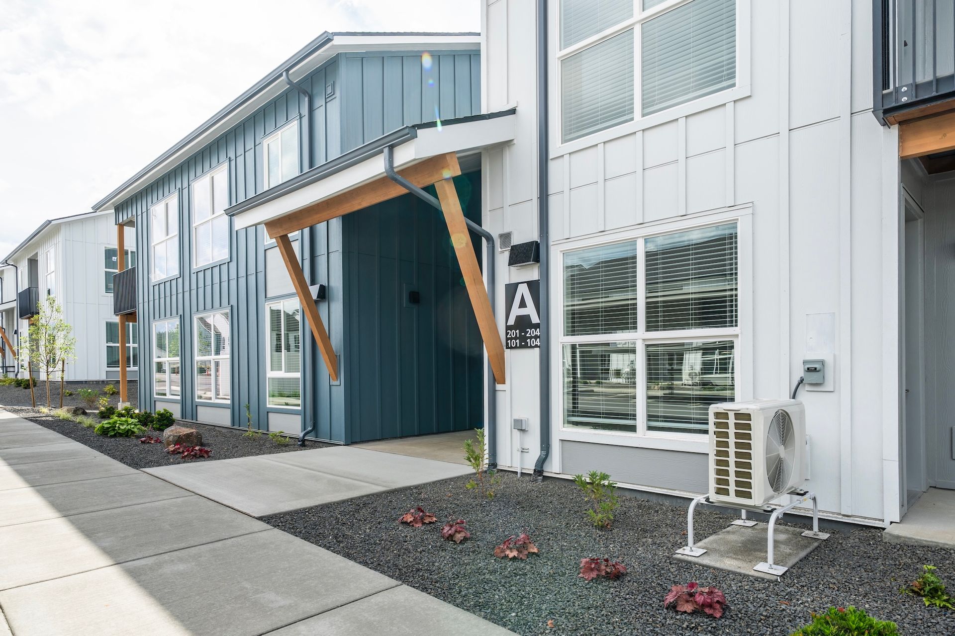 Modern apartment building exterior with gray siding, blue accents, and a landscaped yard.