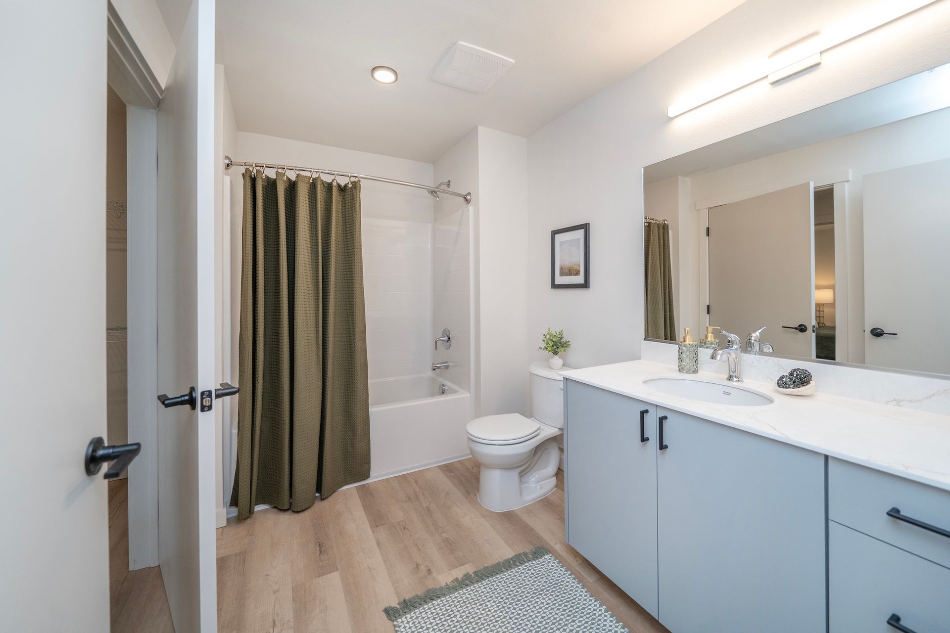 Modern bathroom with light blue cabinets, white countertop, and green shower curtain.