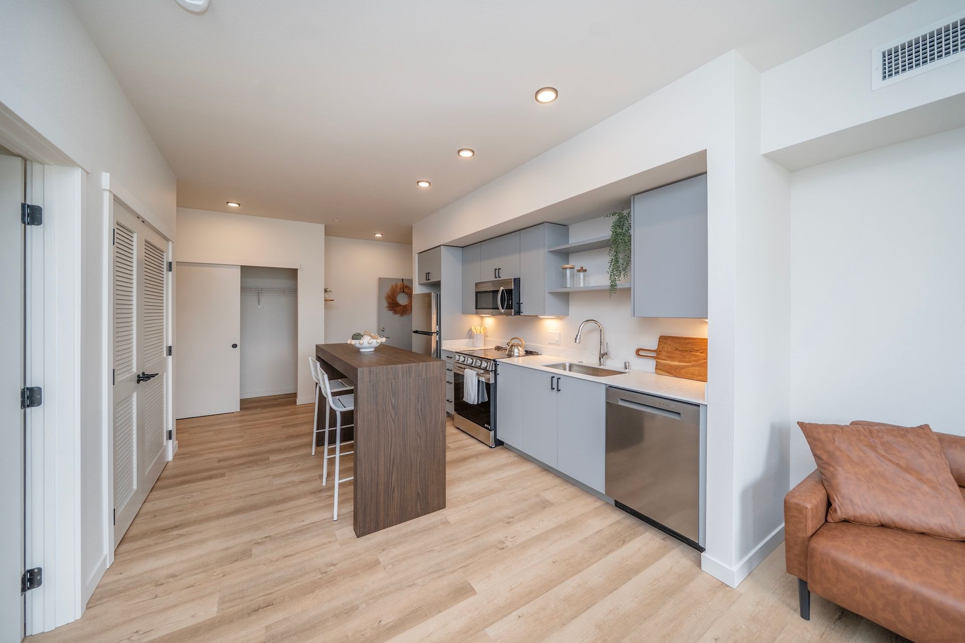 Modern kitchen with island, cabinets, stainless steel appliances, and brown leather couch.
