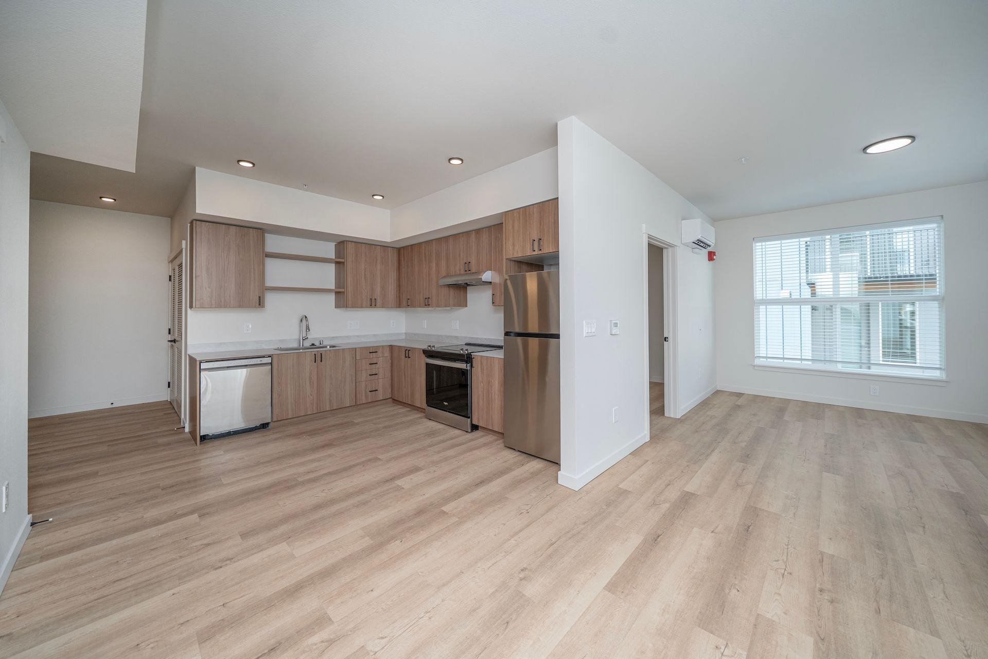 Empty modern apartment with wood floors and kitchen.