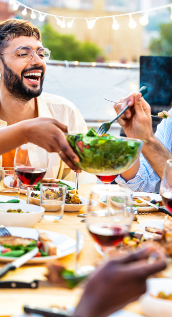 A group of people are sitting at a table eating food and drinking wine.