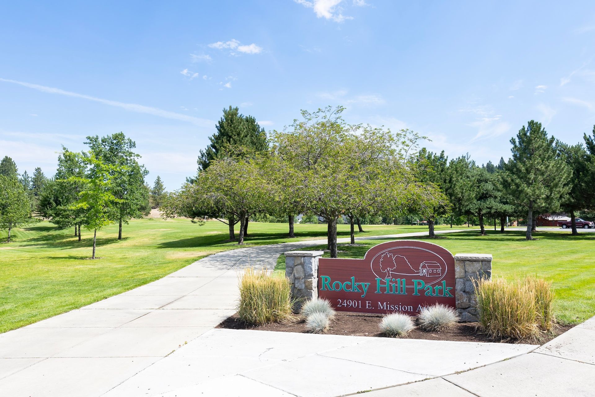 Rocks Hill Park sign with trees and green grass under a blue sky.