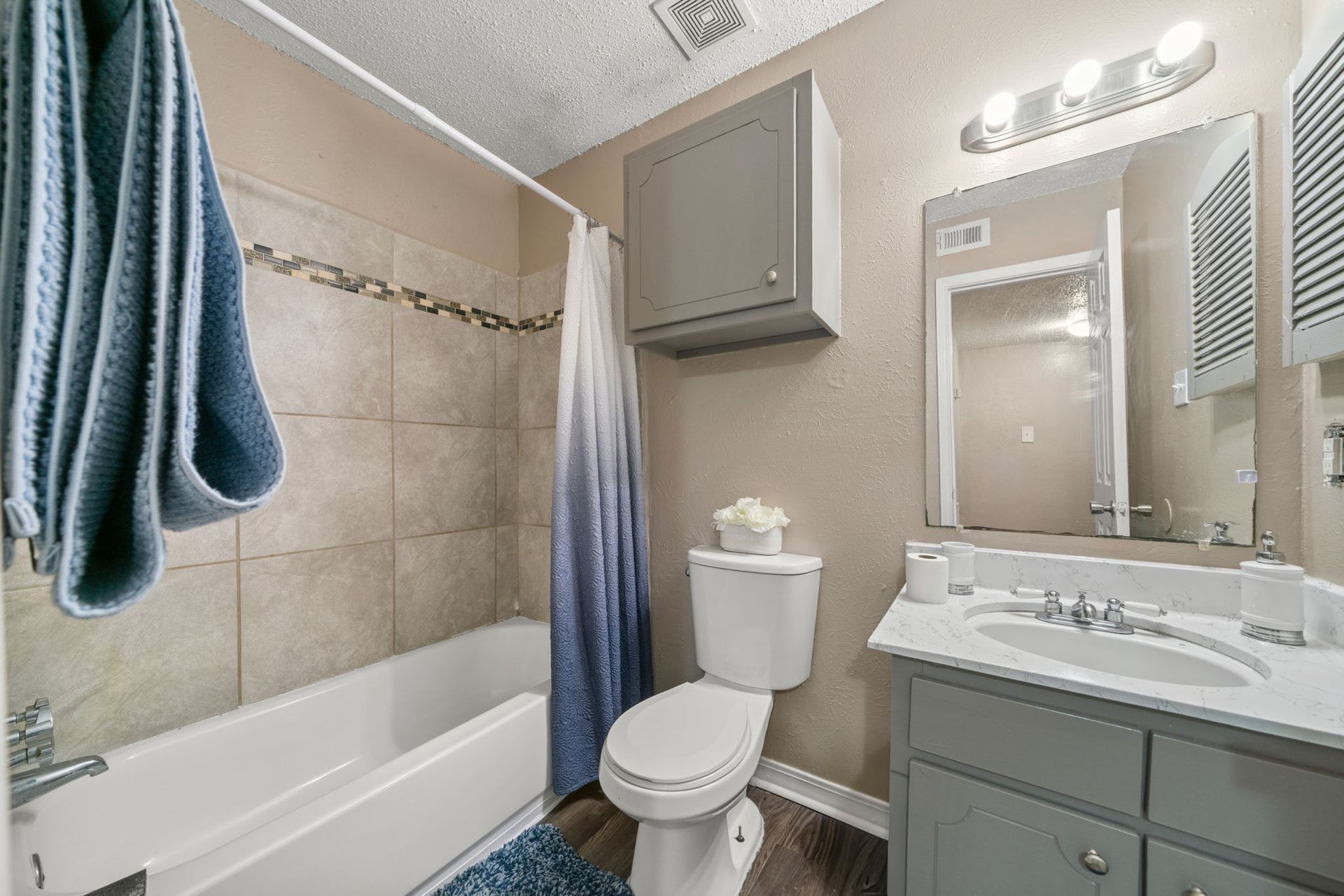 Bathroom with white tub, toilet, and vanity. Blue and beige tones throughout.