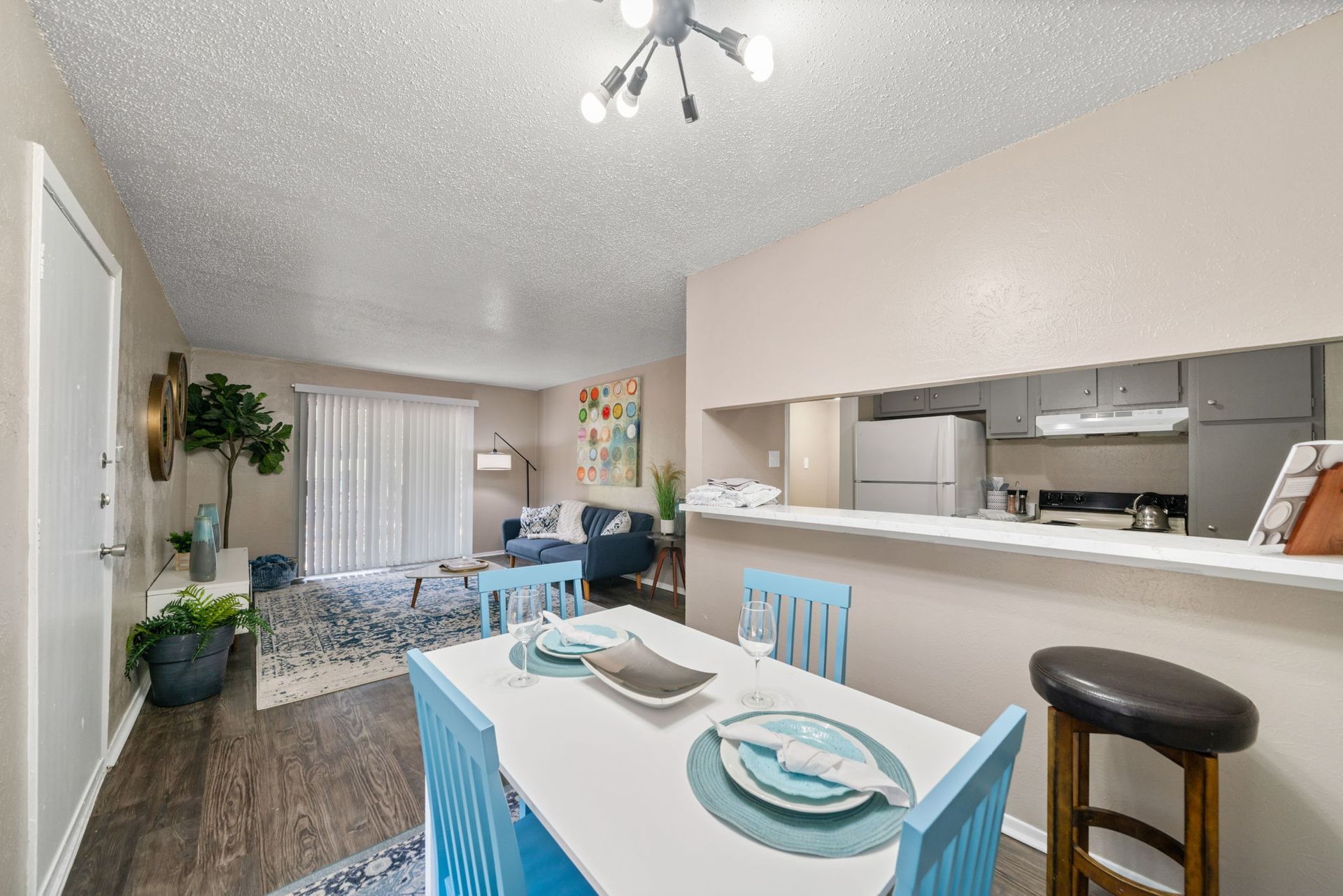 Bright, open dining and living area; blue accents; white table with place settings; kitchen visible.
