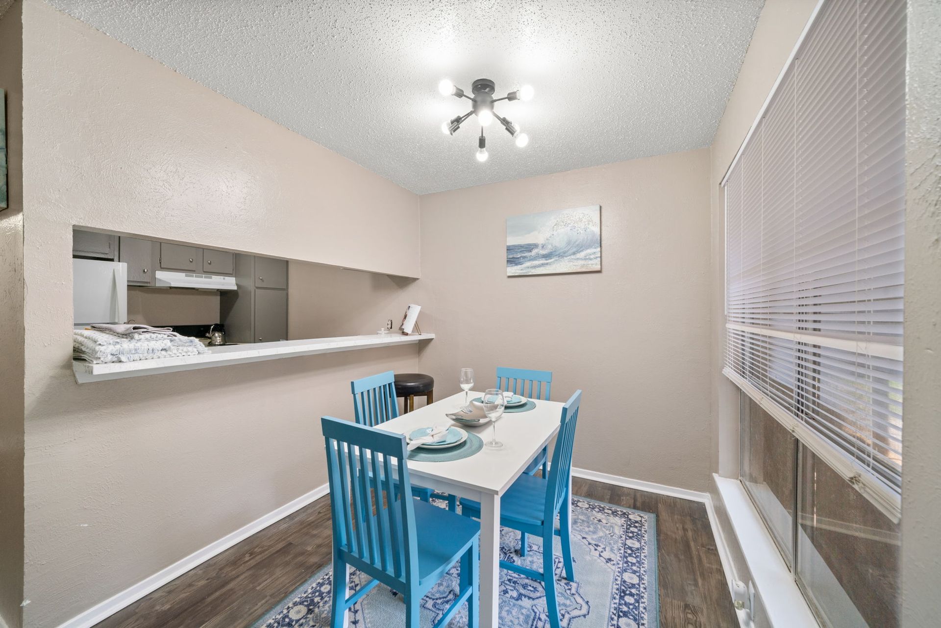 Dining area with a white table, blue chairs, a rug, and a window.
