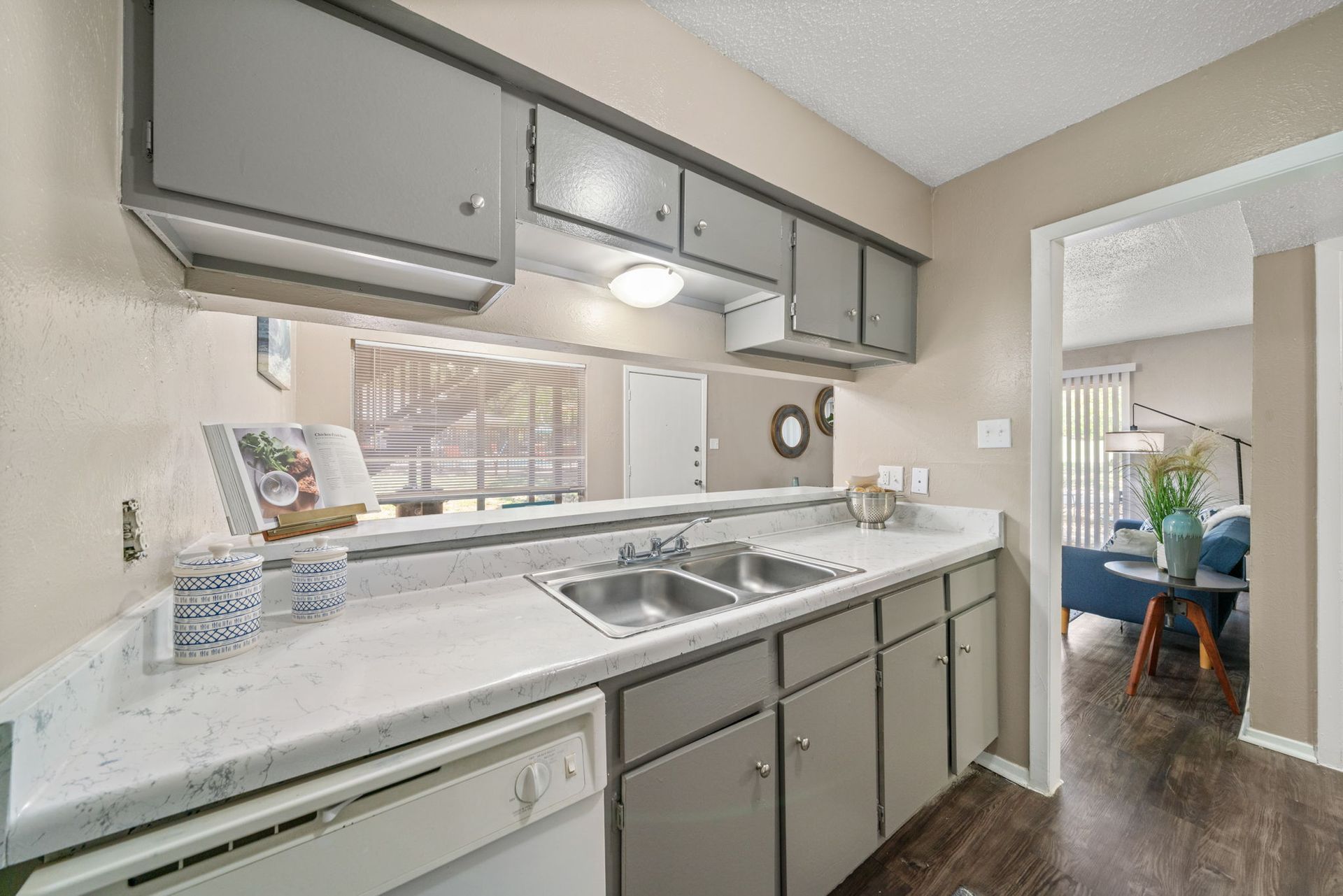 Kitchen with grey cabinets, white countertop, and doorway to living area.