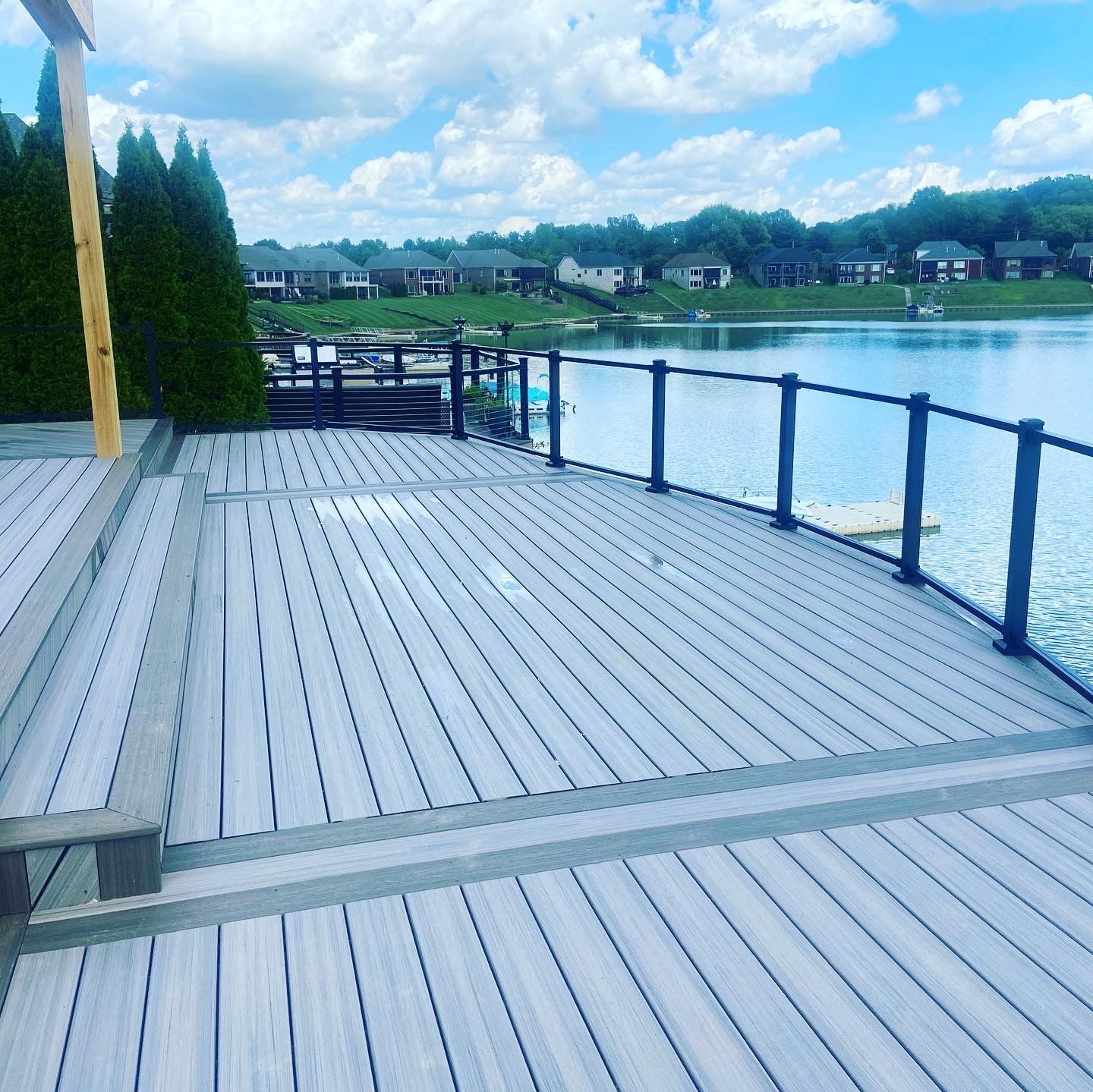 Gray composite deck overlooking a lake with black railing and blue sky.