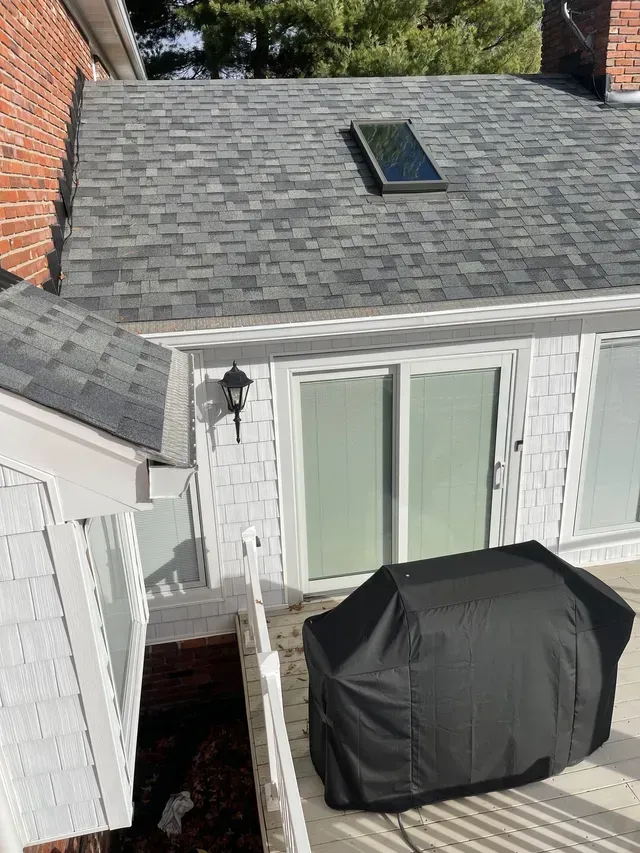 Gray shingled roof with skylight over a white deck with a covered grill, white sliding doors.