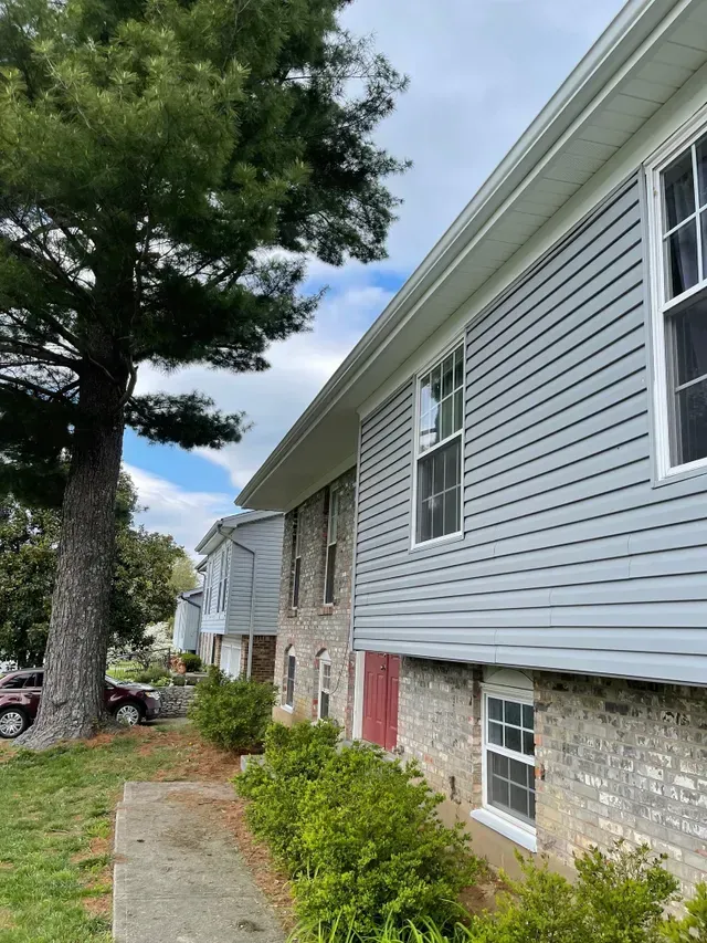 Row of townhouses with gray siding and brick, next to a tree on a grassy lawn.