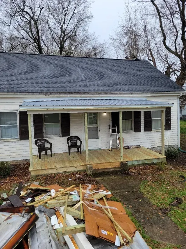 A small, white house with a new wooden porch. Lumber and debris in the foreground. Cloudy sky.