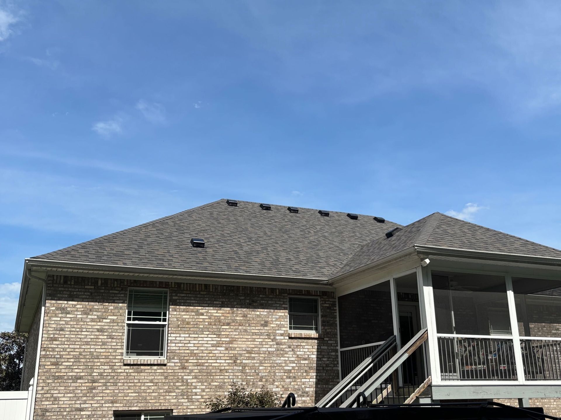 Worker kneeling on a rooftop installing materials beside a gray house wall.