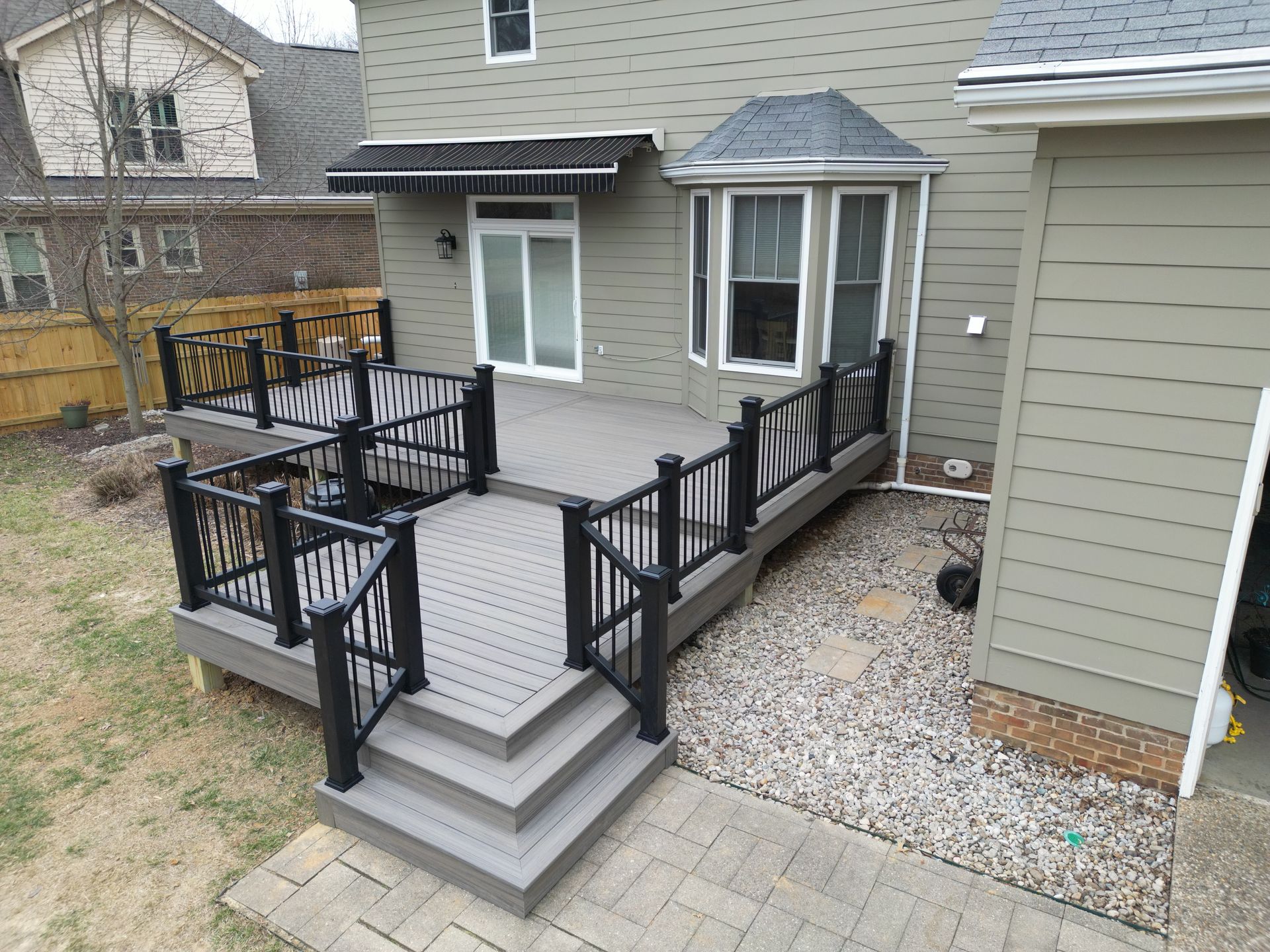 Gray composite deck with black railings and steps in a backyard.