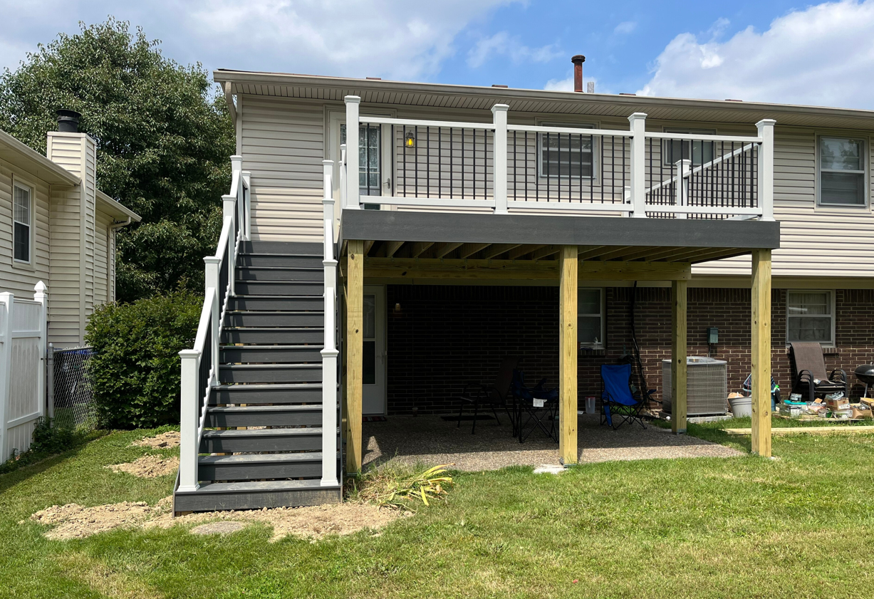 A two-story deck with gray stairs, white railings, and a gravel ground.