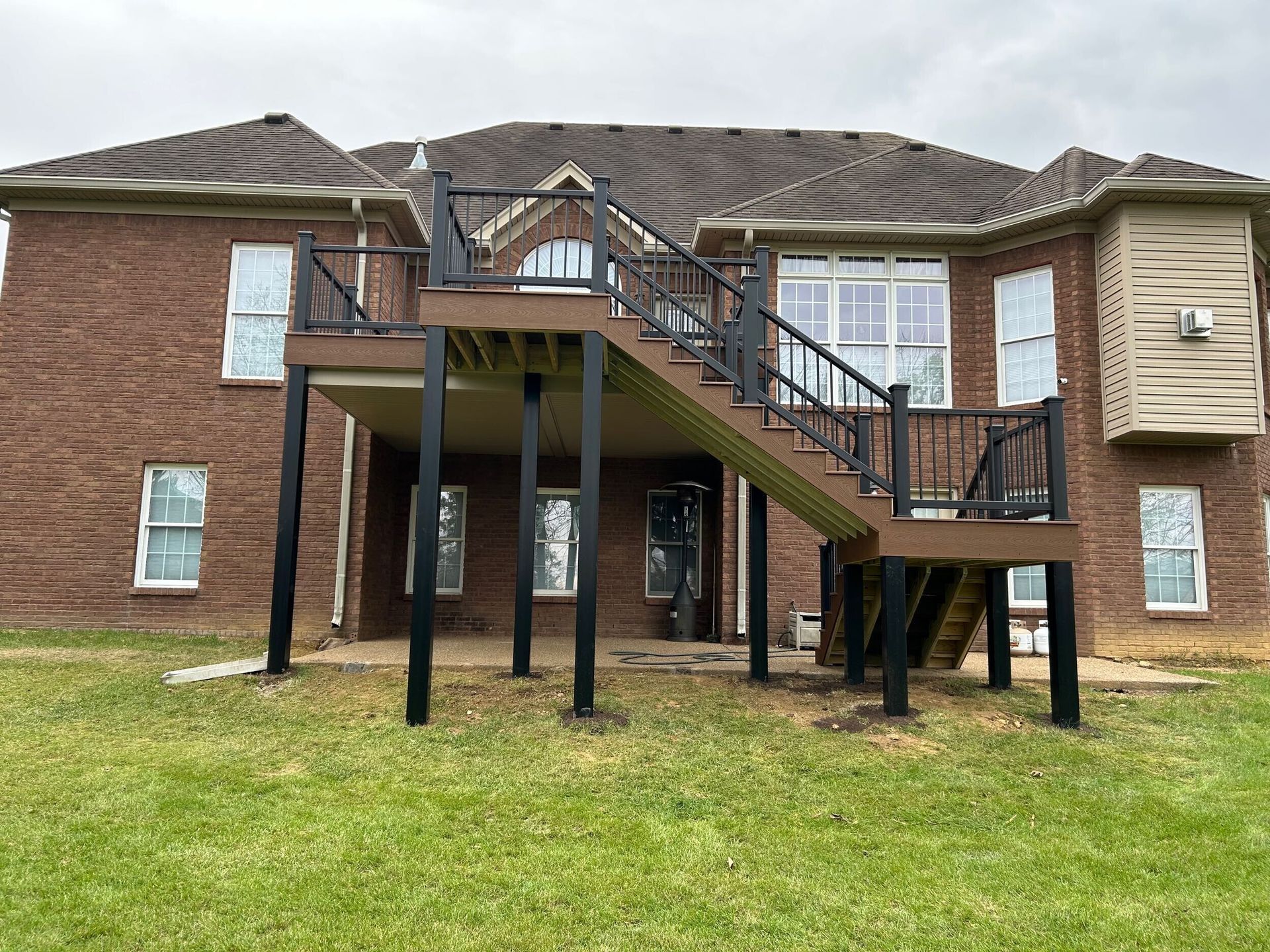 Raised wooden deck with stairs attached to a brick house. Black railings and supports.
