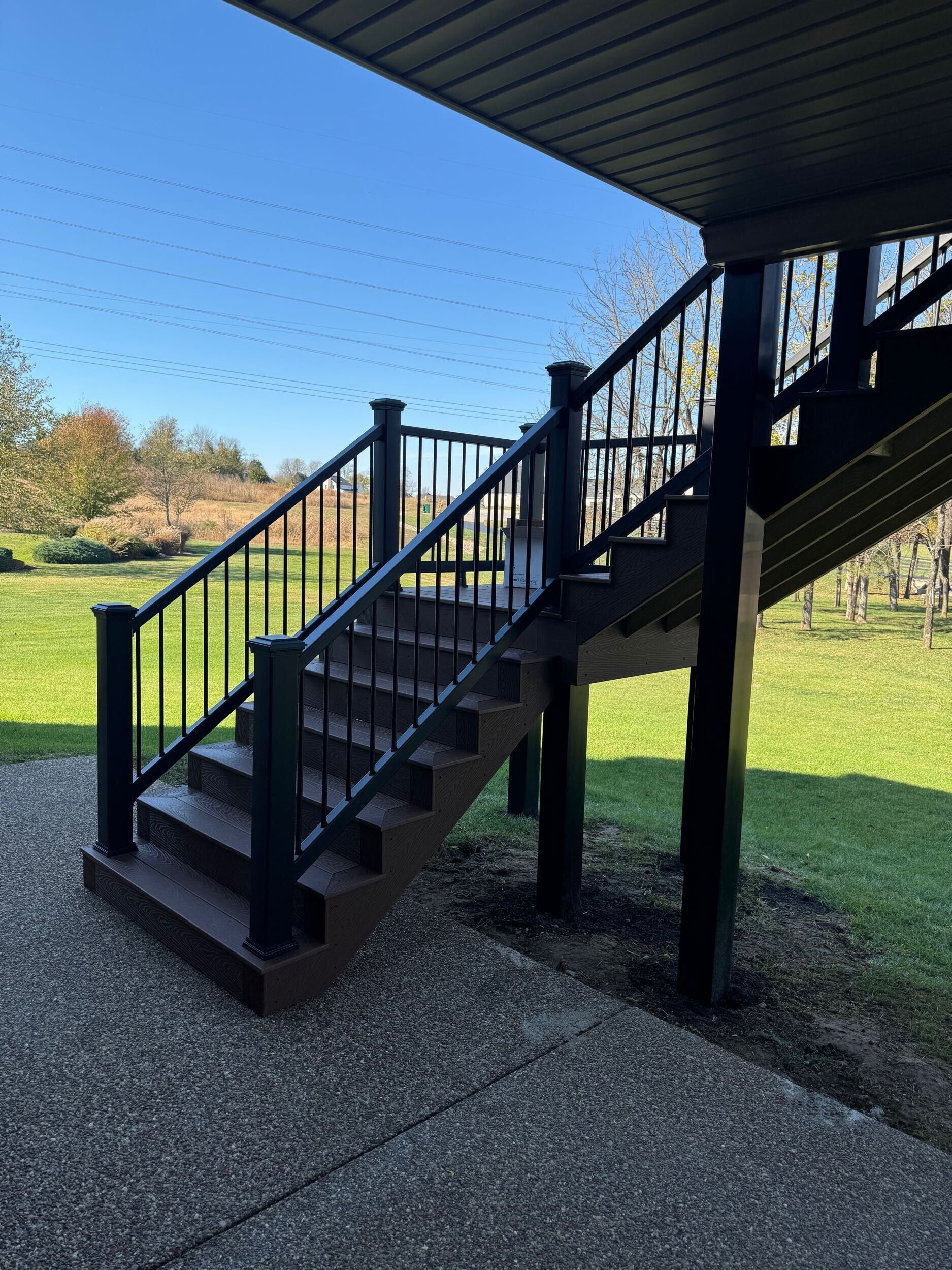 Brown deck stairs with black railing and posts, leading to a grassy yard.