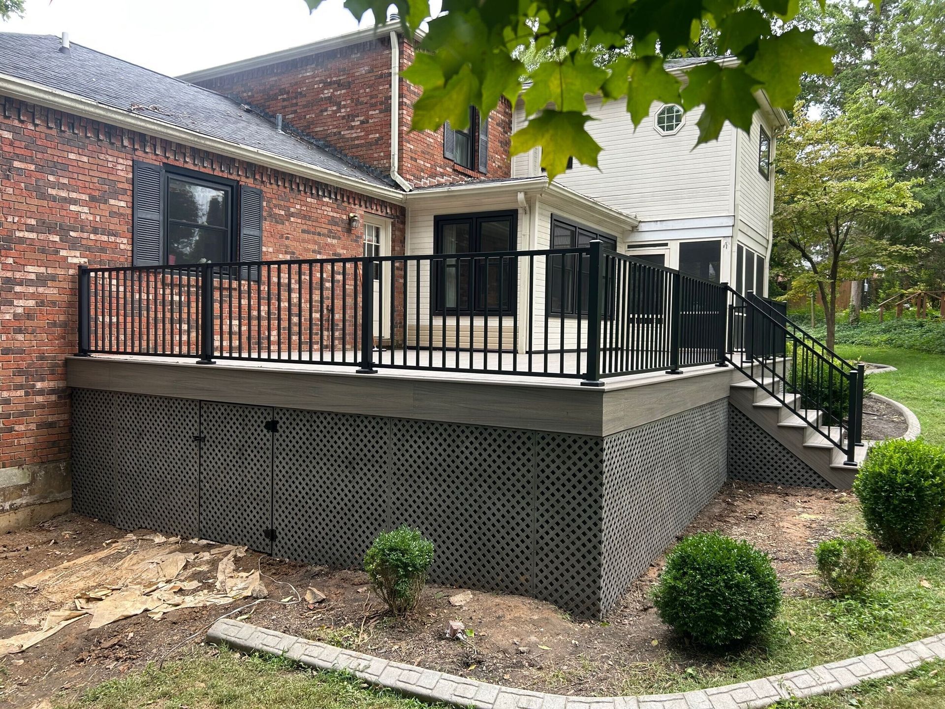 A raised deck with black railings and composite skirting attached to a brick and white house.