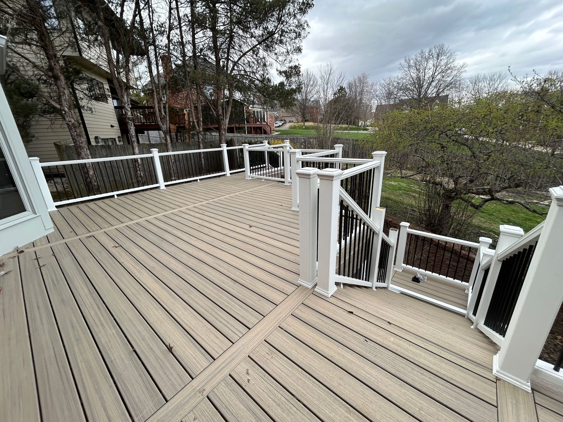 Spacious composite deck with white posts, black railing, and a view of trees and a yard.