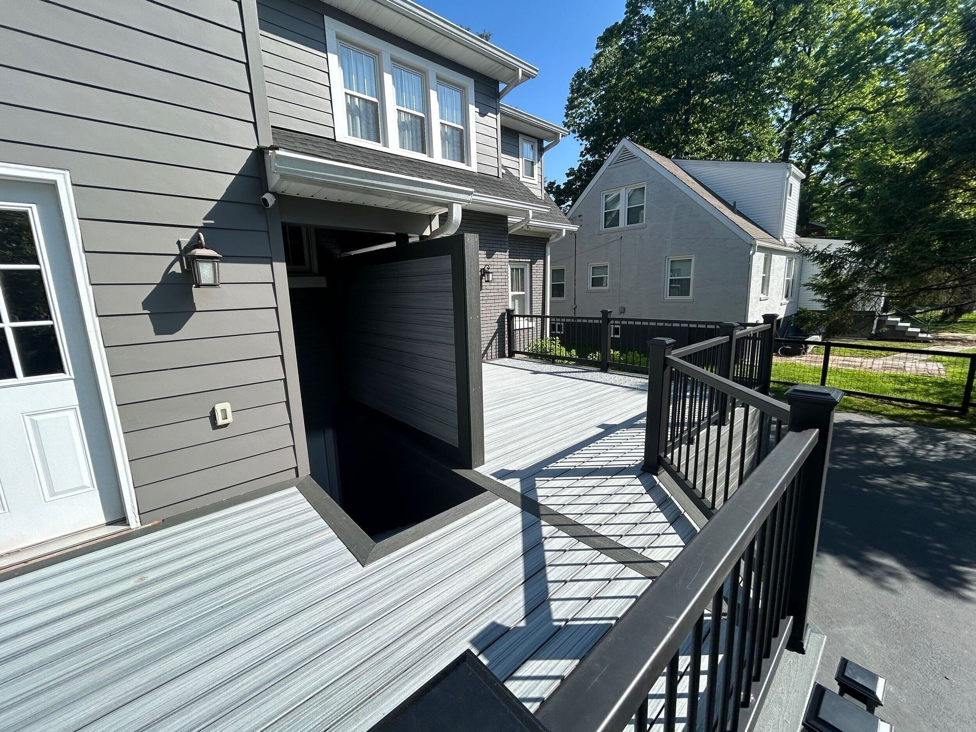 Exterior of a building with a gray deck and ramp. Dark entrance under a canopy. Another building in the background.