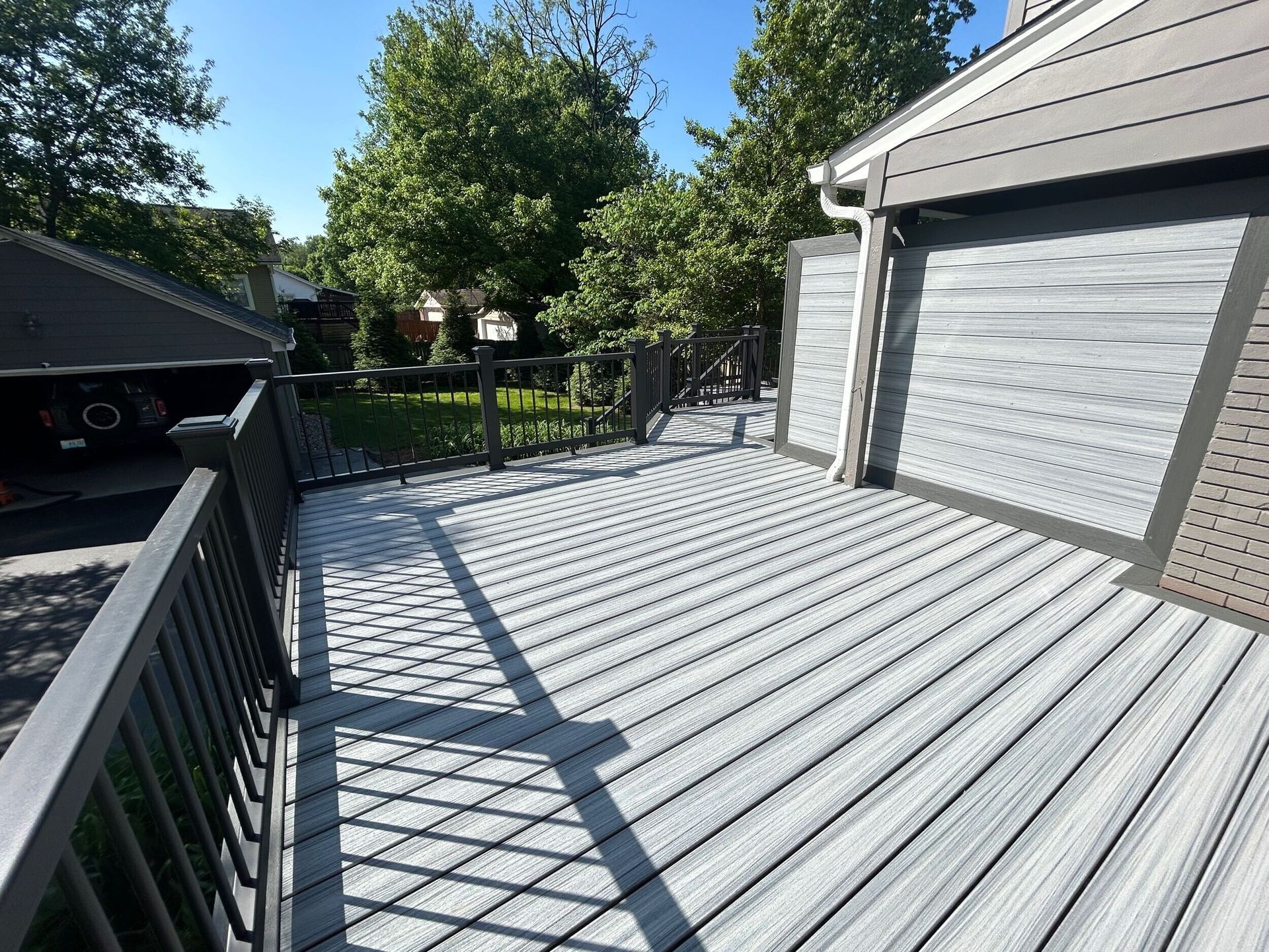 Gray composite deck with black railing, against a house on a sunny day.