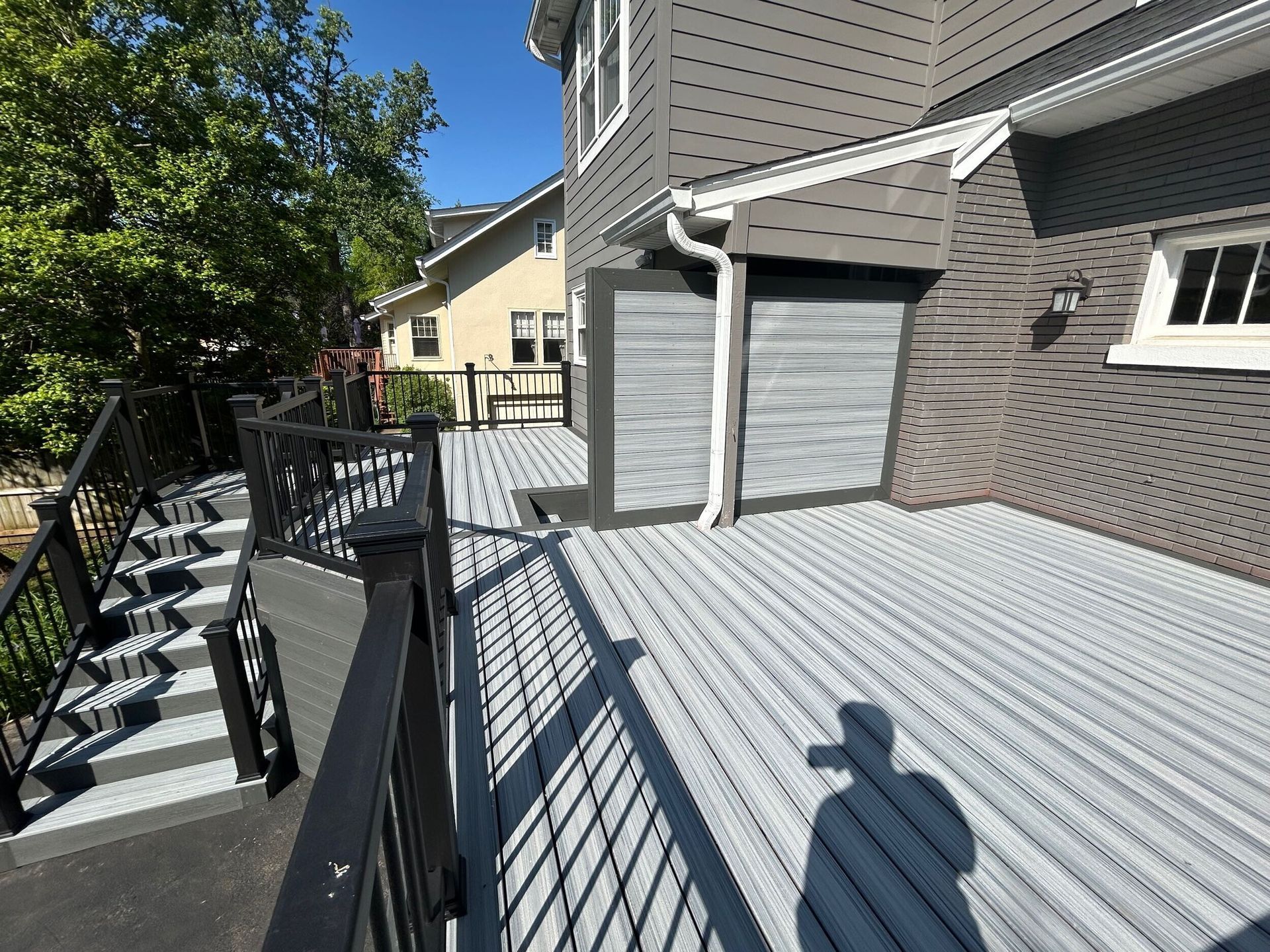 Gray composite deck with black railings and steps leading to a house with gray siding.