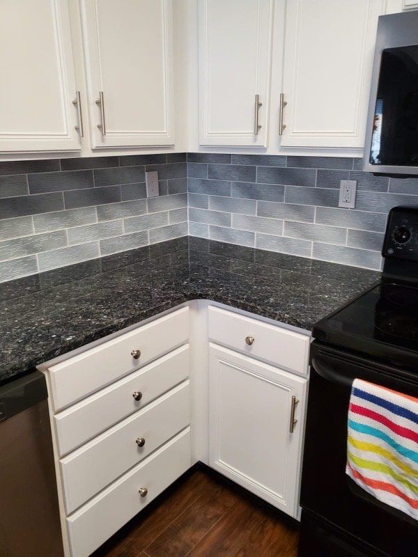 White kitchen cabinets with a black countertop and gray tile backsplash.