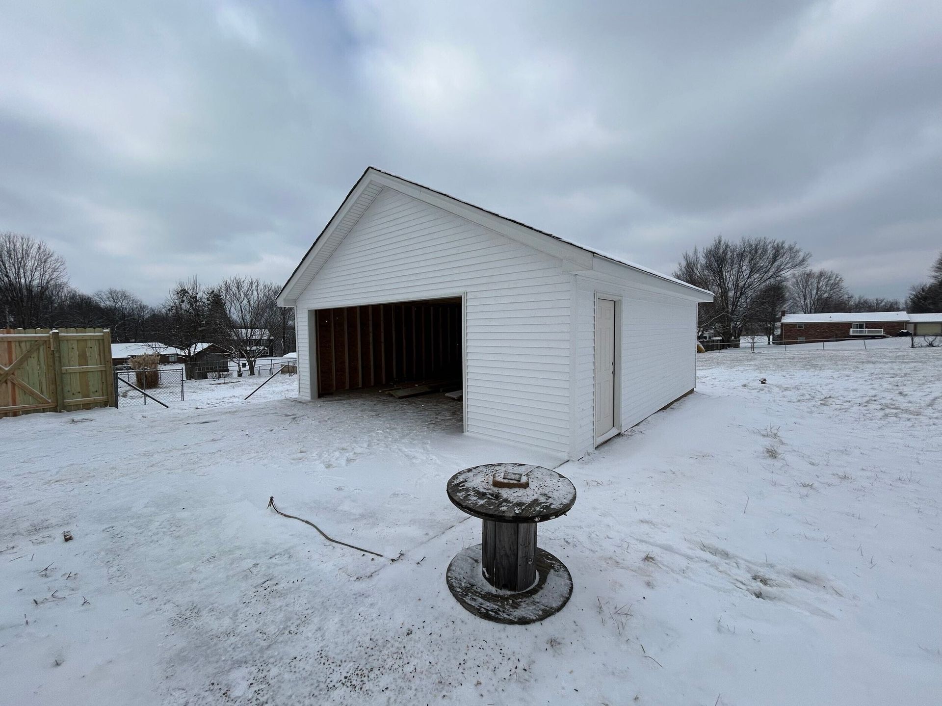 White building with open garage door, construction site in snow.