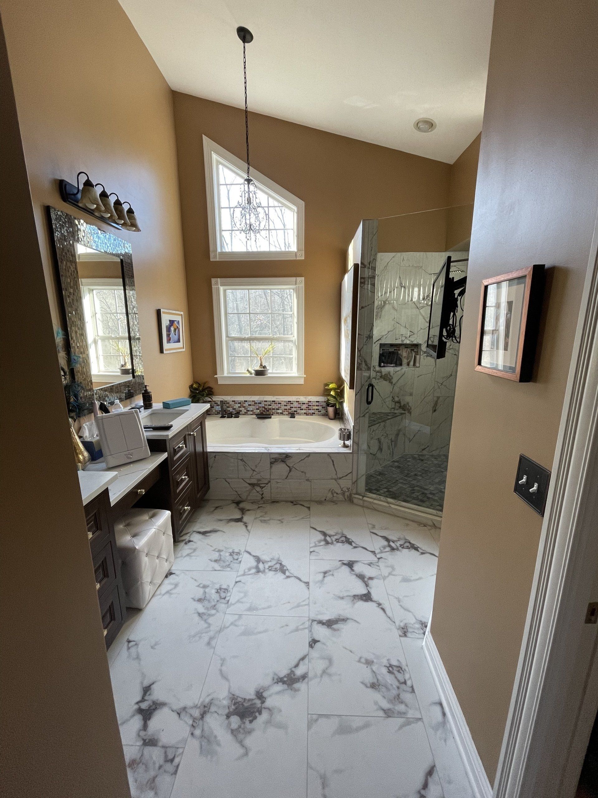 Bathroom with marble floor, bathtub, shower, vanity, and window. Warm-toned walls.