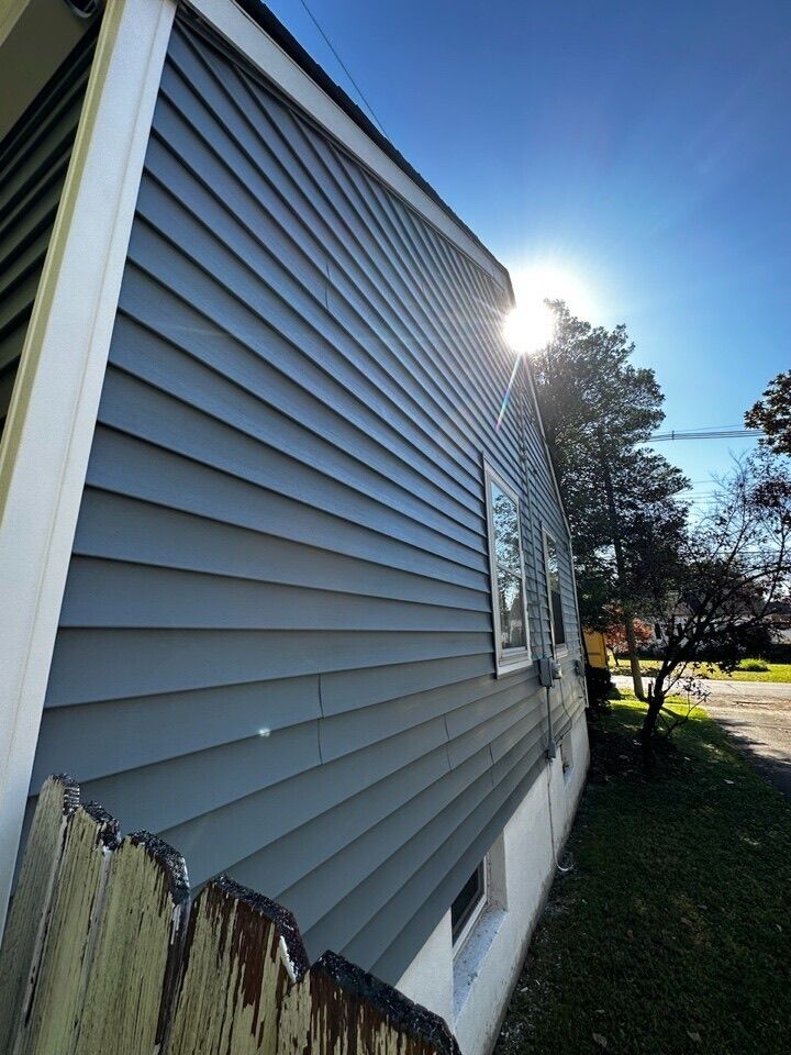 Blue-sided house with white trim under a bright sun; old fence in foreground.