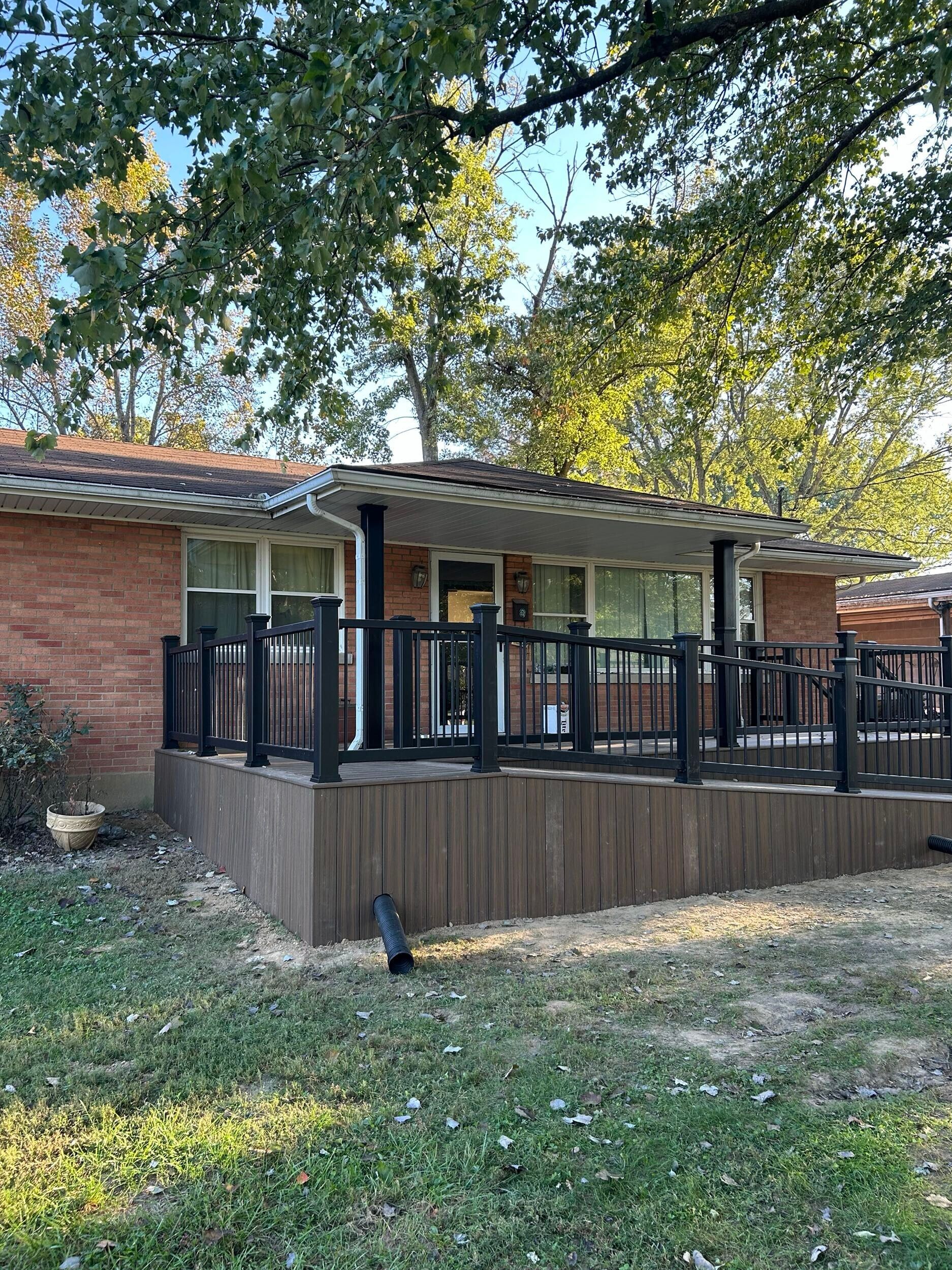 Brick house with a black railing deck and a green lawn.