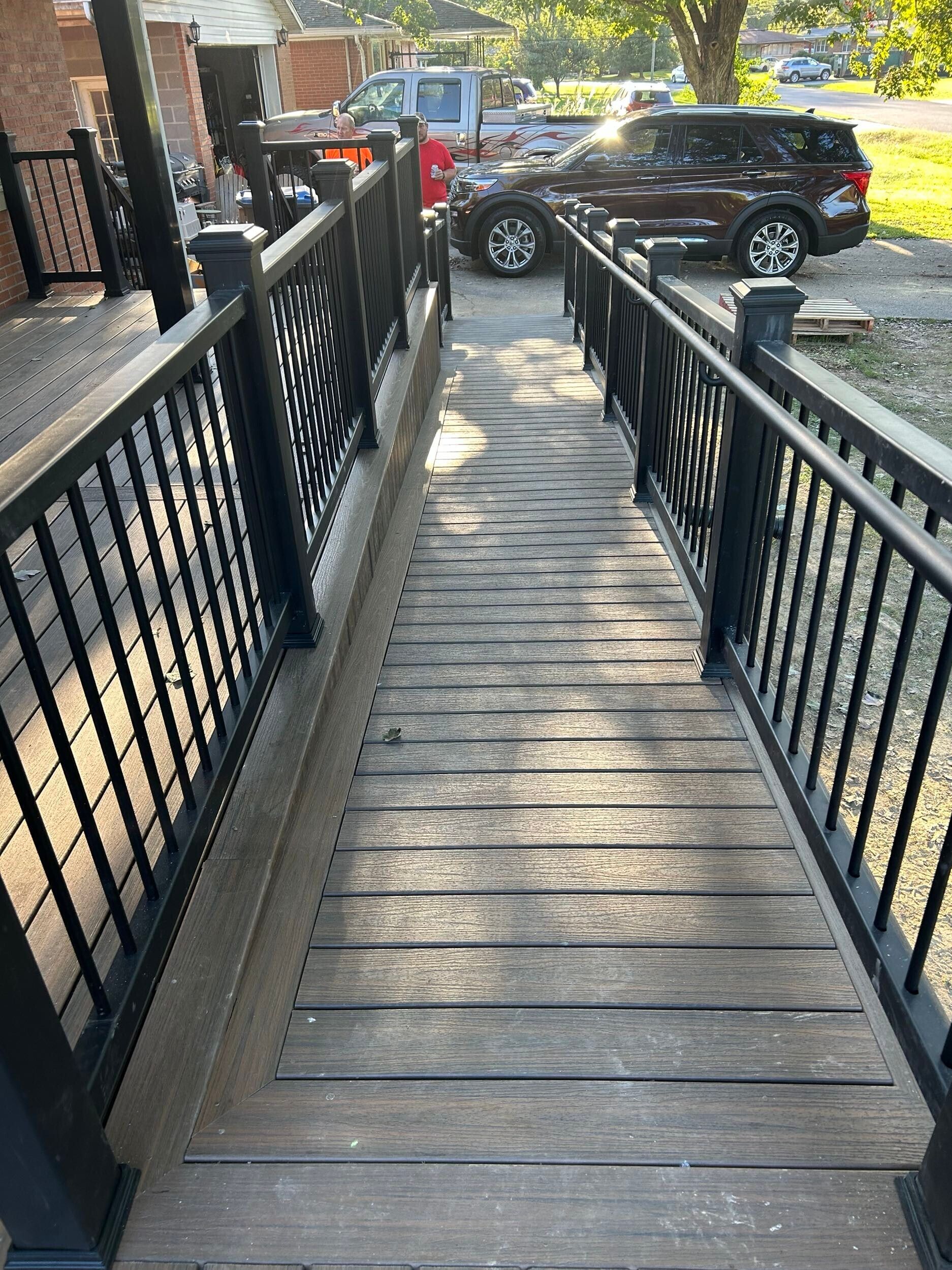 Wooden ramp with black railings, leading up to a building. Cars and trees in background.