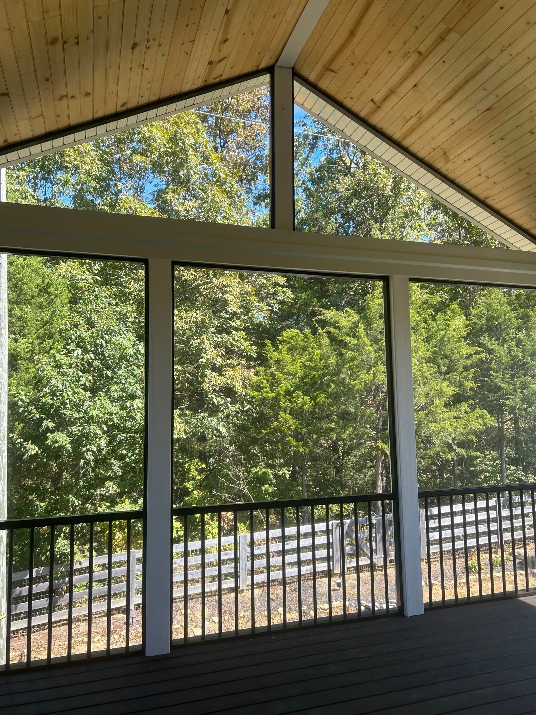 Screened porch with wooden ceiling overlooking a lush green forest.