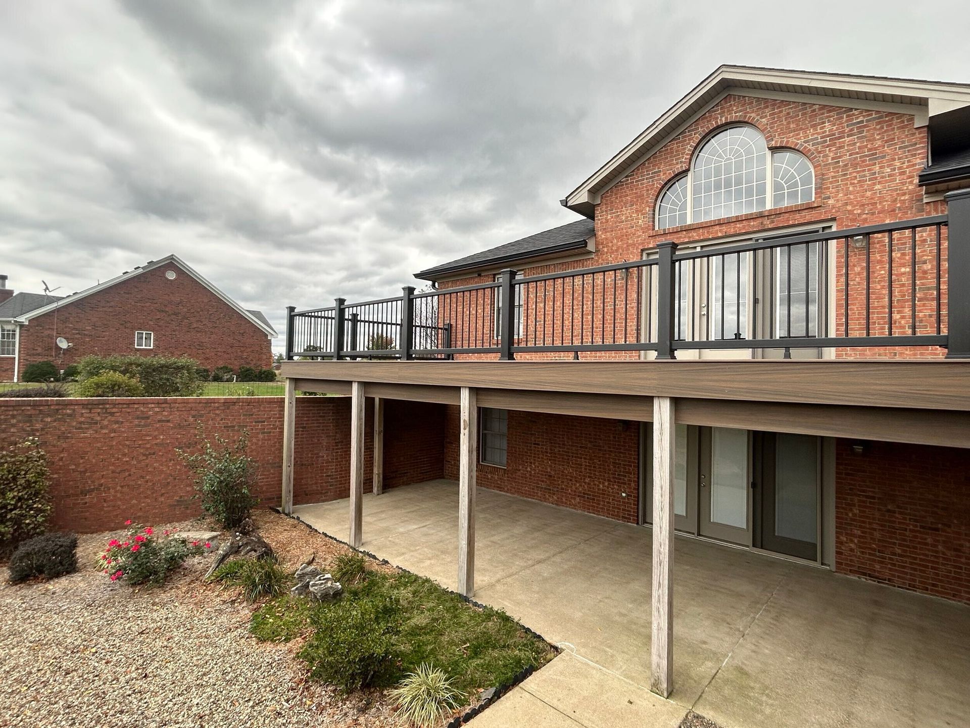 Brick house with deck; cloudy sky. Outdoor patio area below deck, small garden in foreground.