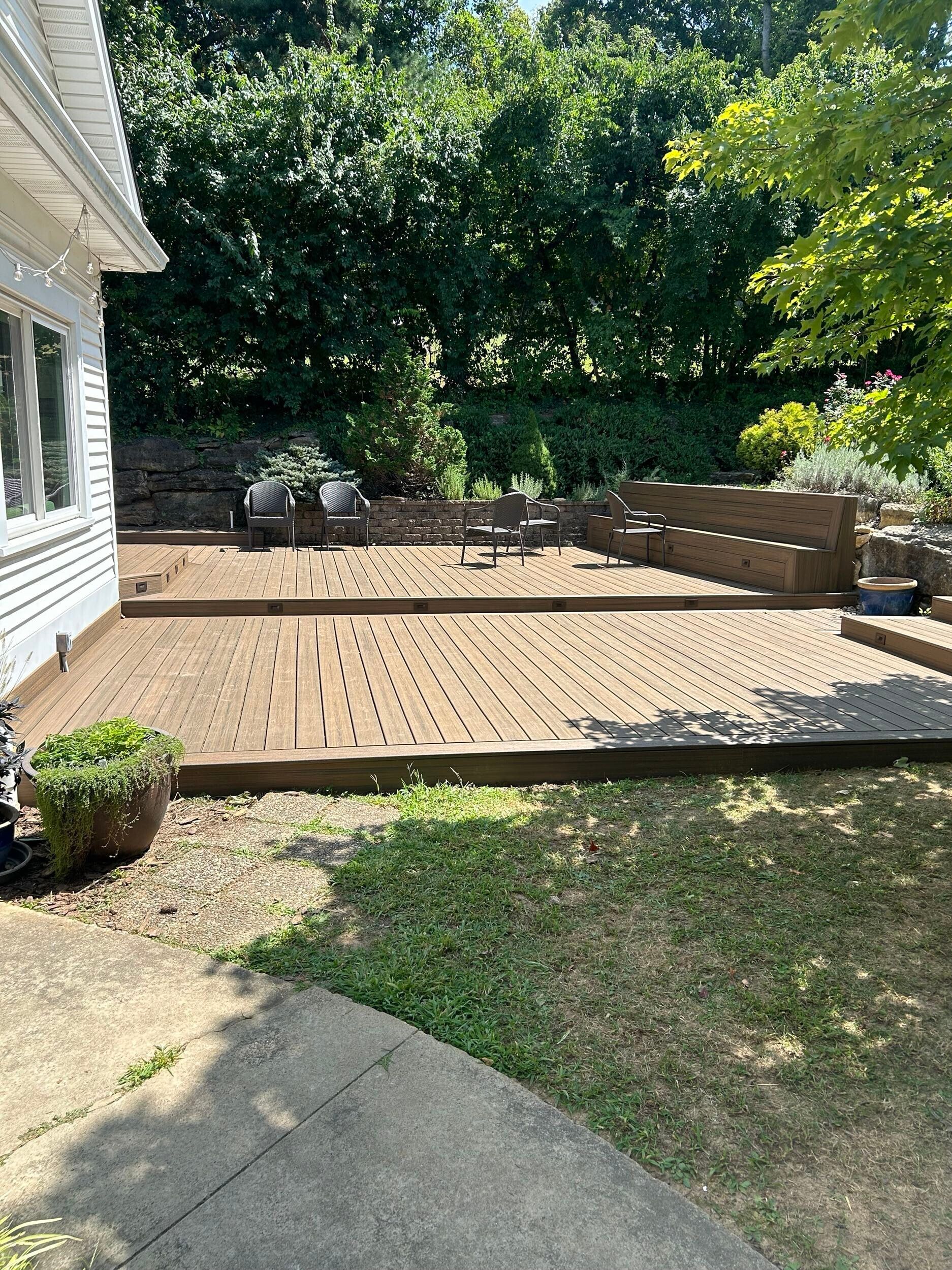Wooden deck with furniture, next to a white house and green lawn.