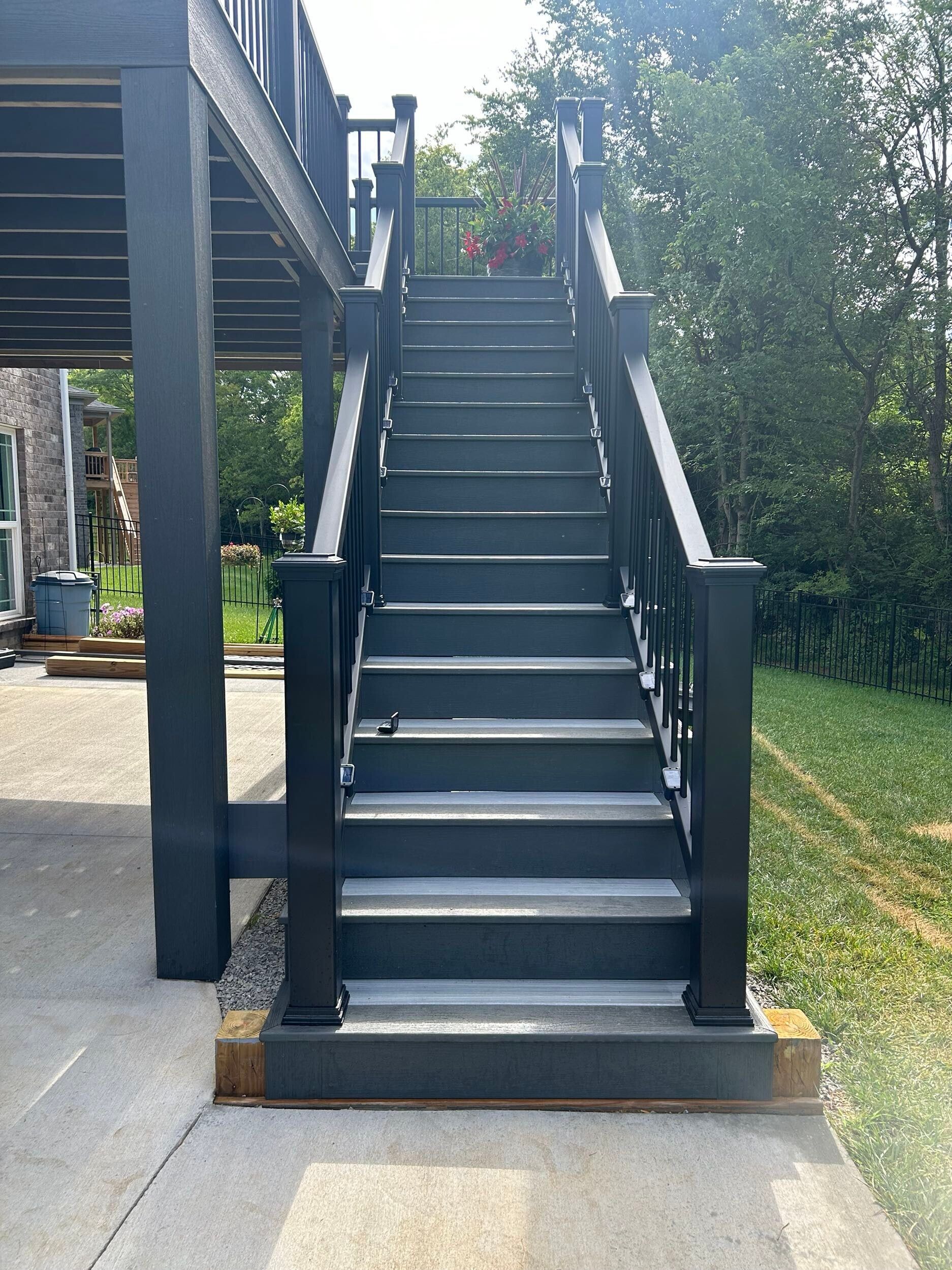 Dark gray outdoor staircase leading up to a deck, with a grassy background.