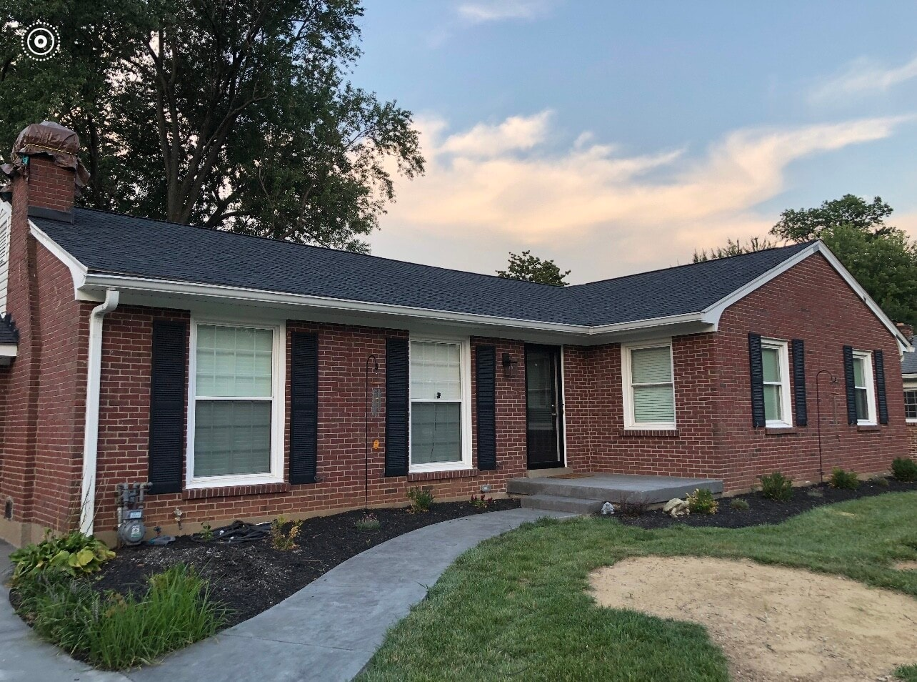 Brick ranch-style house with black shutters, dark roof, and a curved walkway.