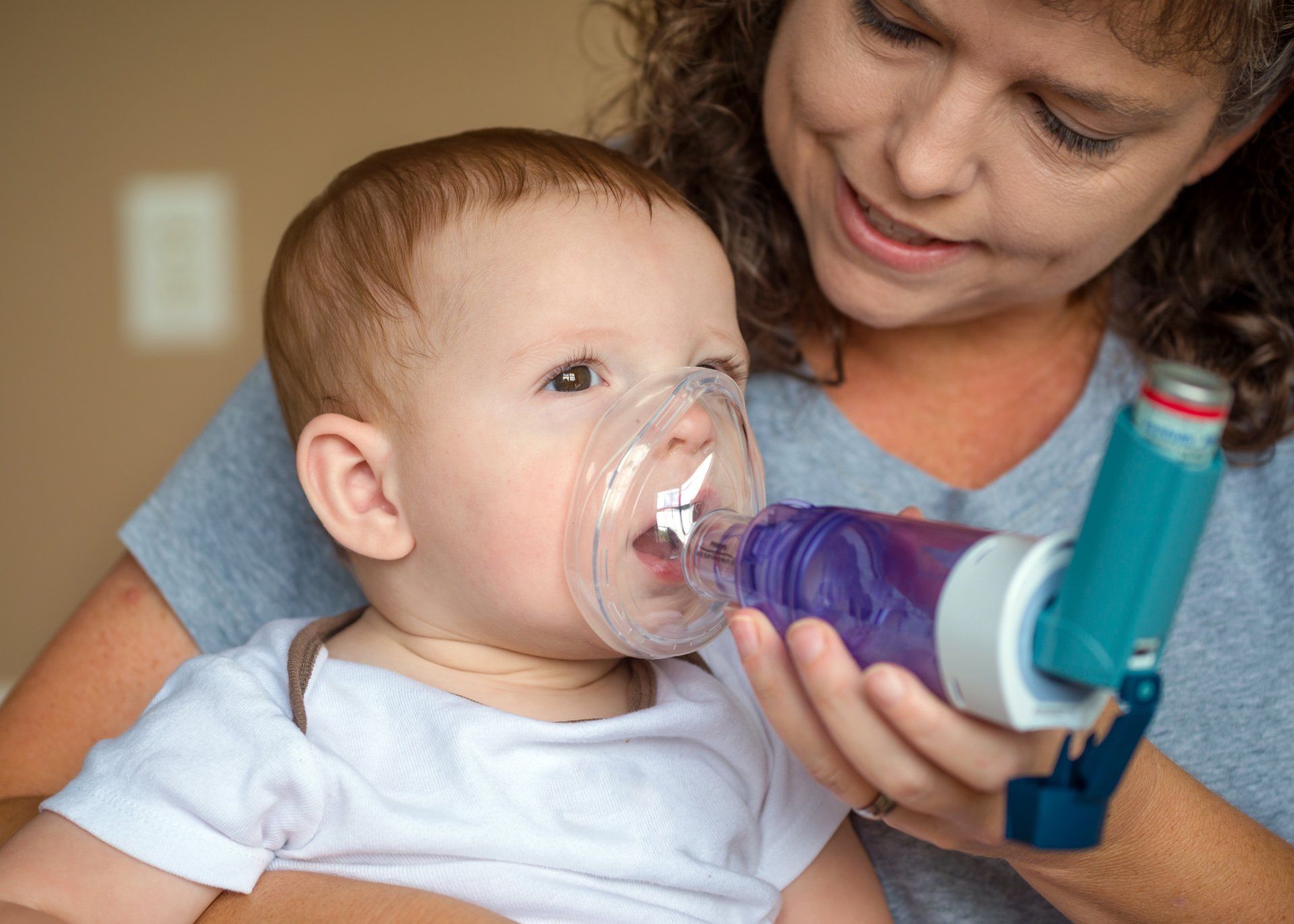 a woman is holding a baby who is using an inhaler
