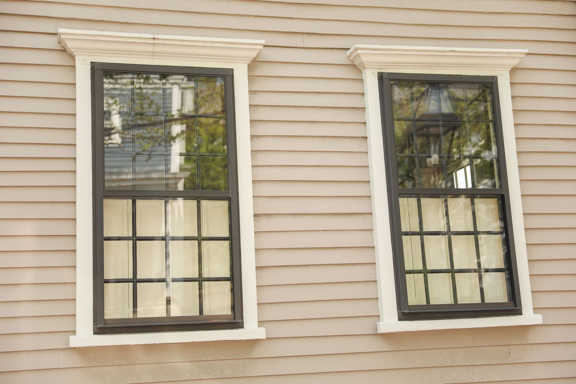 Black grid-style double-hung windows installed on beige siding of a residential home