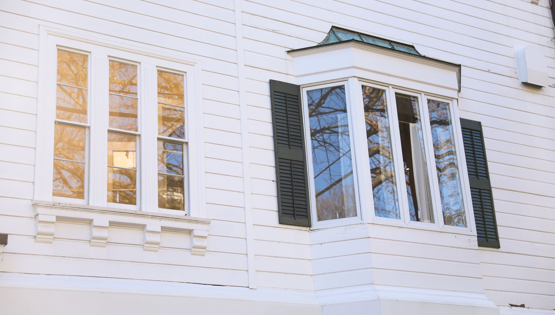 White house exterior with double-hung and bay windows reflecting tree branches