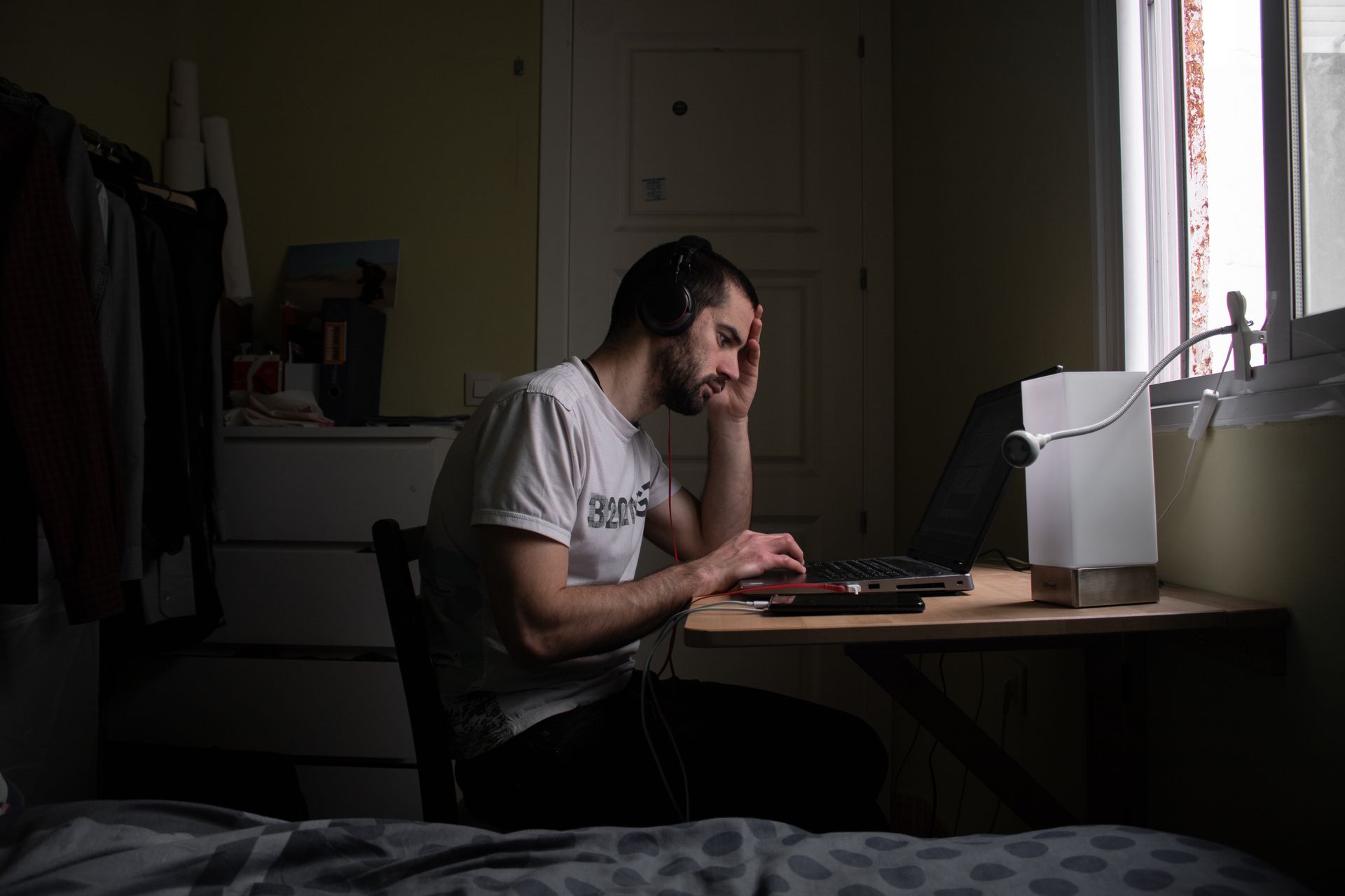 A young white man is focused on teleworking in his bedroom
