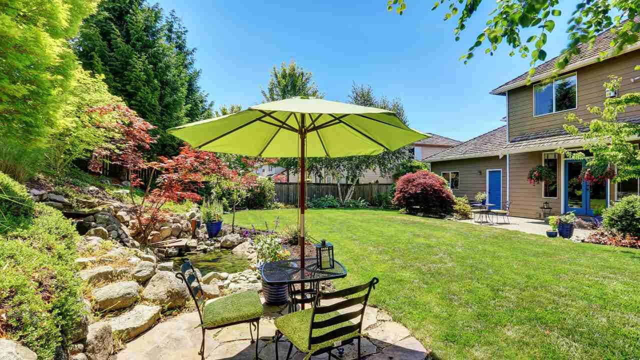 A backyard with a patio and umbrella, surrounded by greenery.