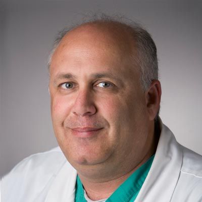 A smiling doctor in a lab coat with a stethoscope around his neck.