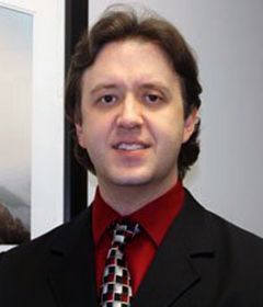 A smiling doctor in a lab coat with a stethoscope around his neck.